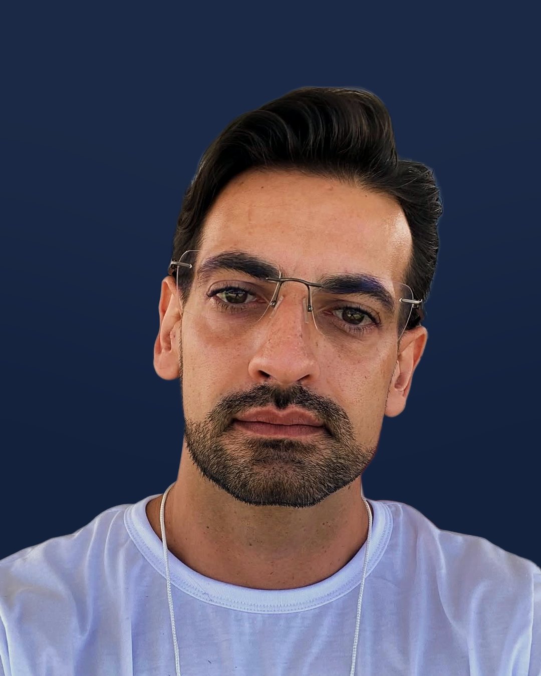 Henrique Reis, de óculos e camiseta branca, olhando para a câmera